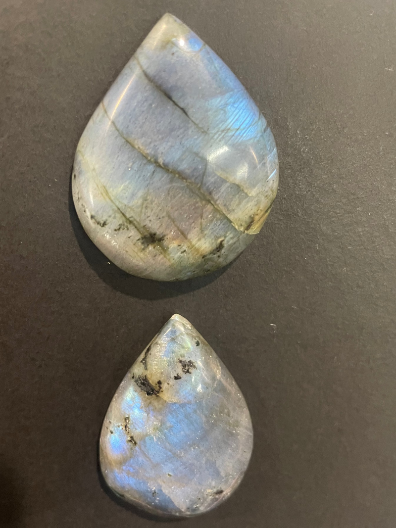 Two teardrop-shaped labradorite stones on a dark surface
