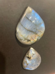 Two teardrop-shaped labradorite stones on a dark surface