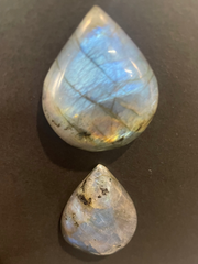 Two teardrop-shaped labradorite stones on a dark surface