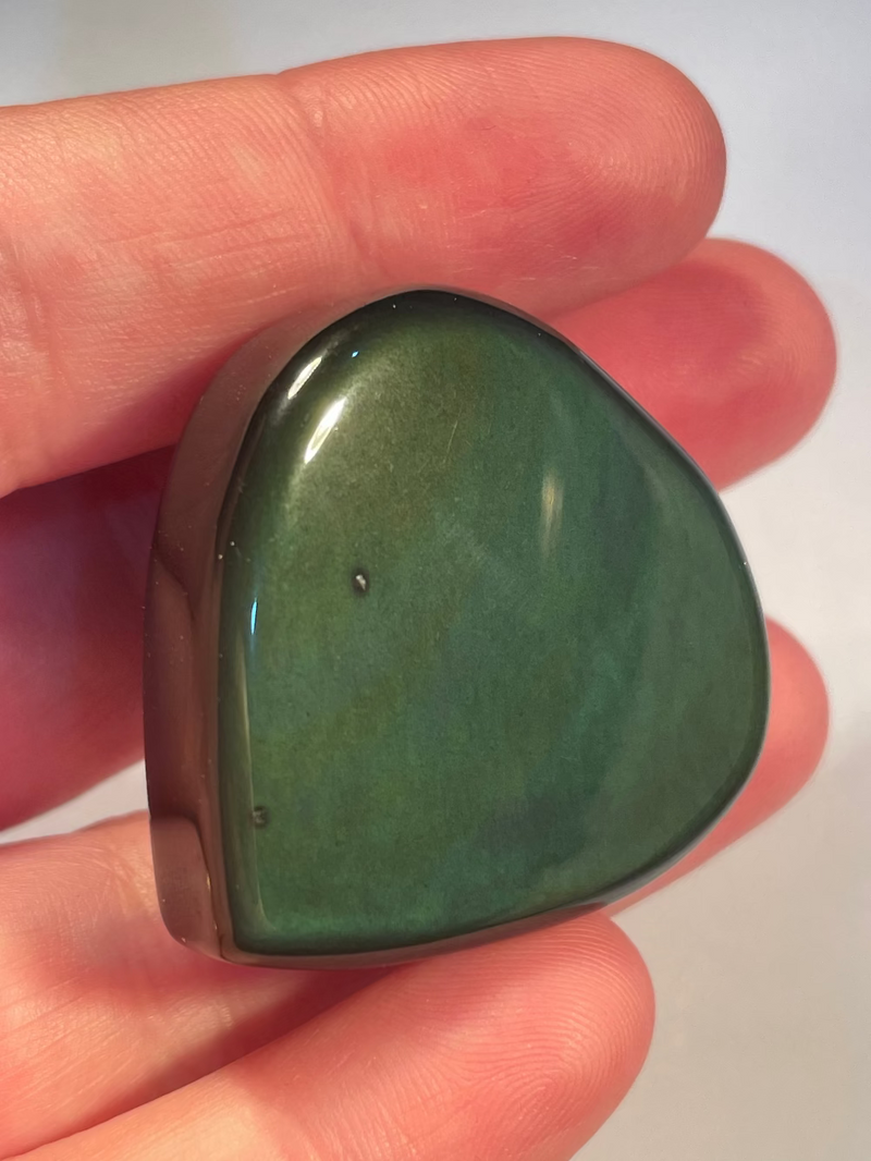 Heart-shaped rainbow obsidian held in a hand against a light background