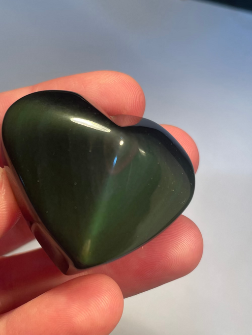 Heart-shaped rainbow obsidian held in a hand against a light background