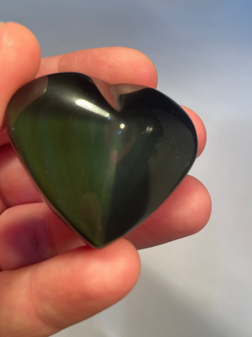 Heart-shaped rainbow obsidian held in a hand against a light background