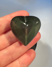 Heart-shaped rainbow obsidian held in a hand against a light background