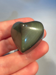 Heart-shaped rainbow obsidian held in a hand against a light background