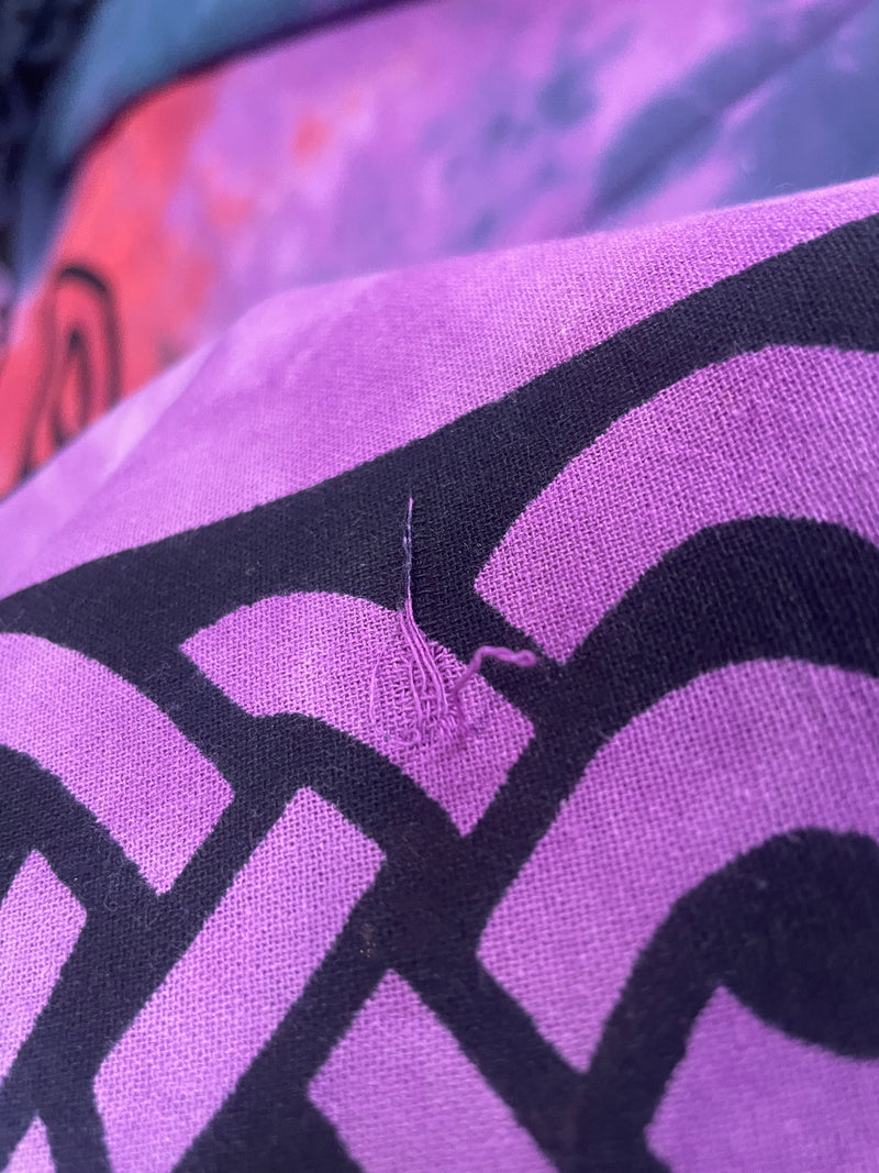 Close-up of a purple and black patterned fabric with a small visible thread snag or tear near the center.