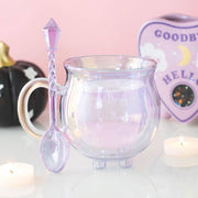 Iridescent glass mug with a decorative spoon on a pink background